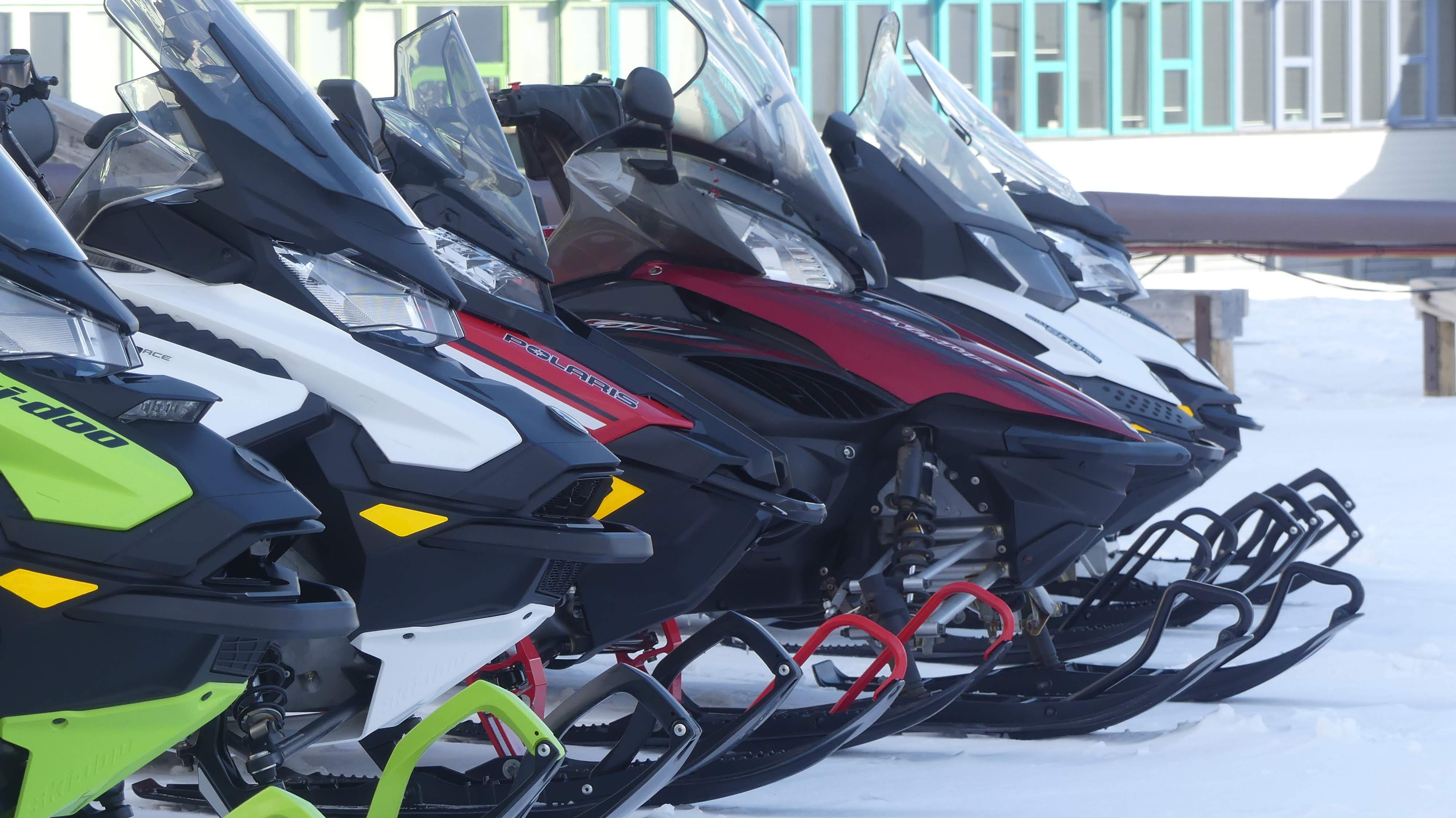 A line of parked skidoos on snow